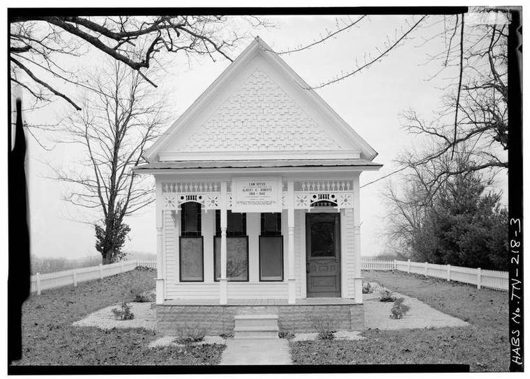 Clean, symmetrical front-elevation view of the law office's Victorian porch, gable, and 'Law Office of Albert H. Roberts, 1868-1946' plaque, with picket fence and lawn.