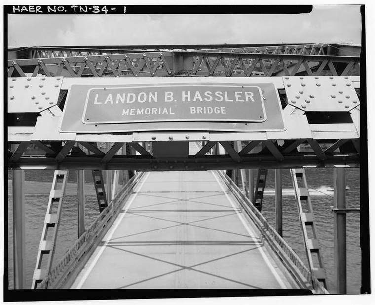 View along the deck of a steel-truss highway bridge crossing the Obey River, framed by its overhead truss and the 'Landon B. Hassler Memorial Bridge' sign, with the impounded river below.
