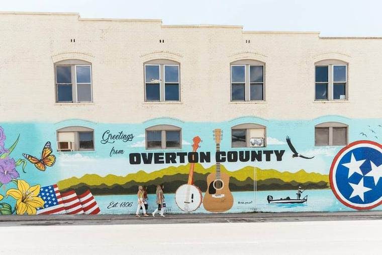 A painted brick wall reading Greetings from Overton County, Est. 1806, with a banjo, a guitar, an eagle, a bass boat and the Tennessee tri-star