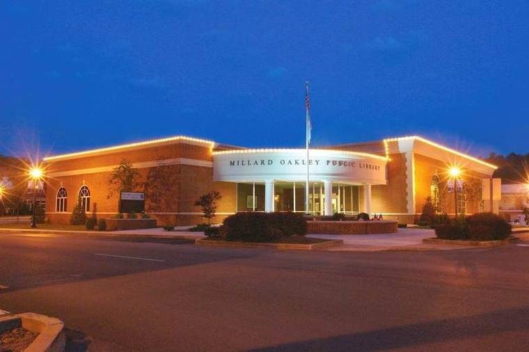 Exterior of Millard Oakley Public Library at dusk with lit building and American flag in front.