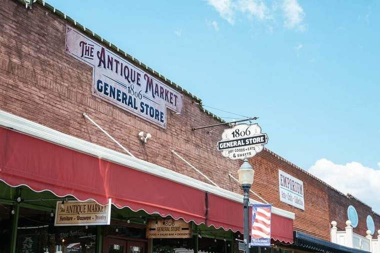 Brick building with signs for The Antique Market and General Store, offering furniture, jewelry, herbs and crafts. Blue sky with some clouds.