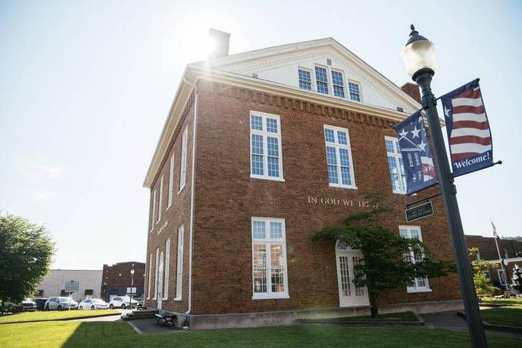 The courthouse in late sun, IN GOD WE TRUST carved into the brick, Welcome banners on the lamp post and a historical marker across the lawn