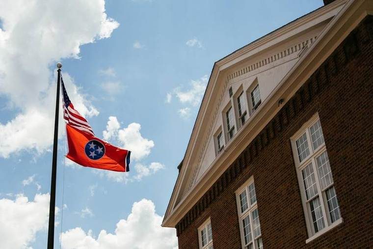 American flag and Tennessee state flag flying outside a brick building under a partly cloudy sky.
