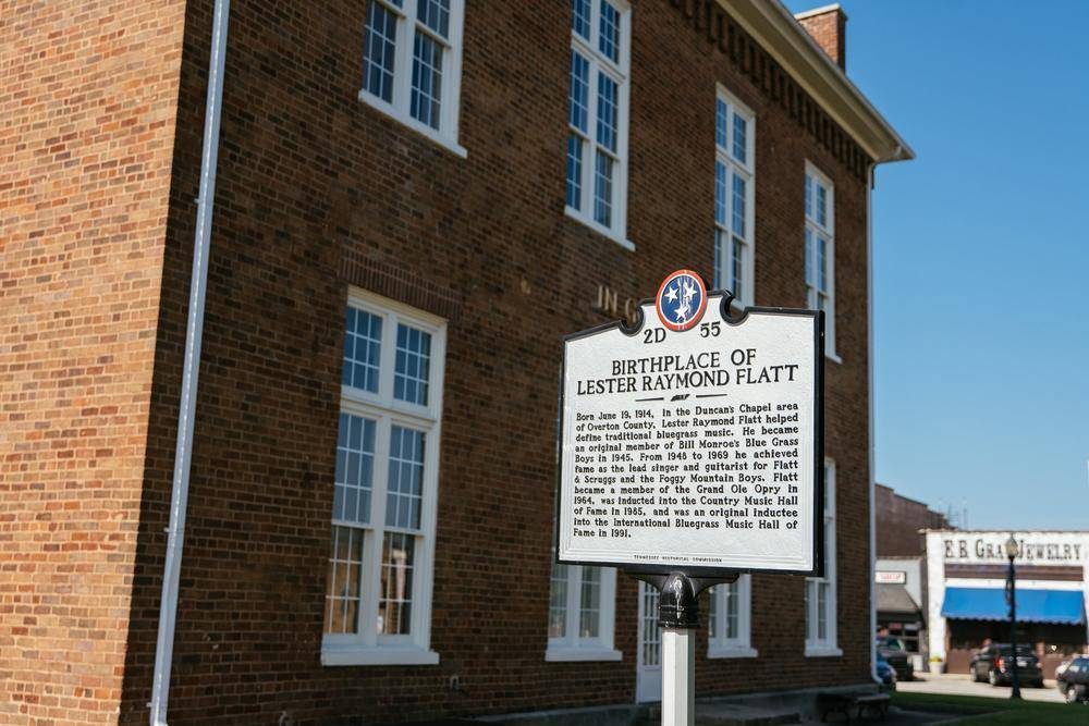 State marker 2D 55, Birthplace of Lester Raymond Flatt, standing in front of the courthouse with E.B. Gray Jewelry on the square behind it