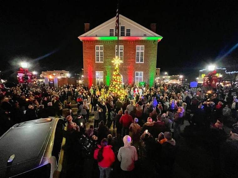 The Overton County Courthouse lit red and green at night, a lit Christmas tree in front of it and the square packed with people