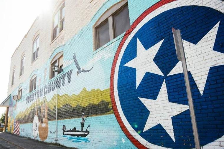 A colorful mural painted on a brick building wall featuring various images, including a boat, a bird, and a large circle with white stars and a red outline.